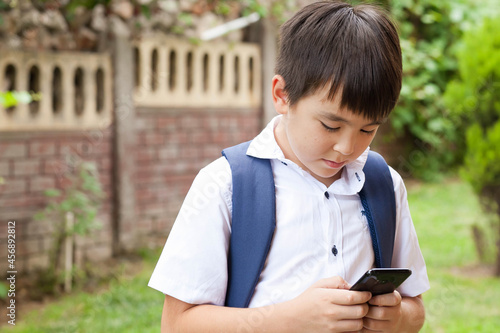  Cute asian schoolboy boy writes a message on the phone outdoors. Communication and gadgets