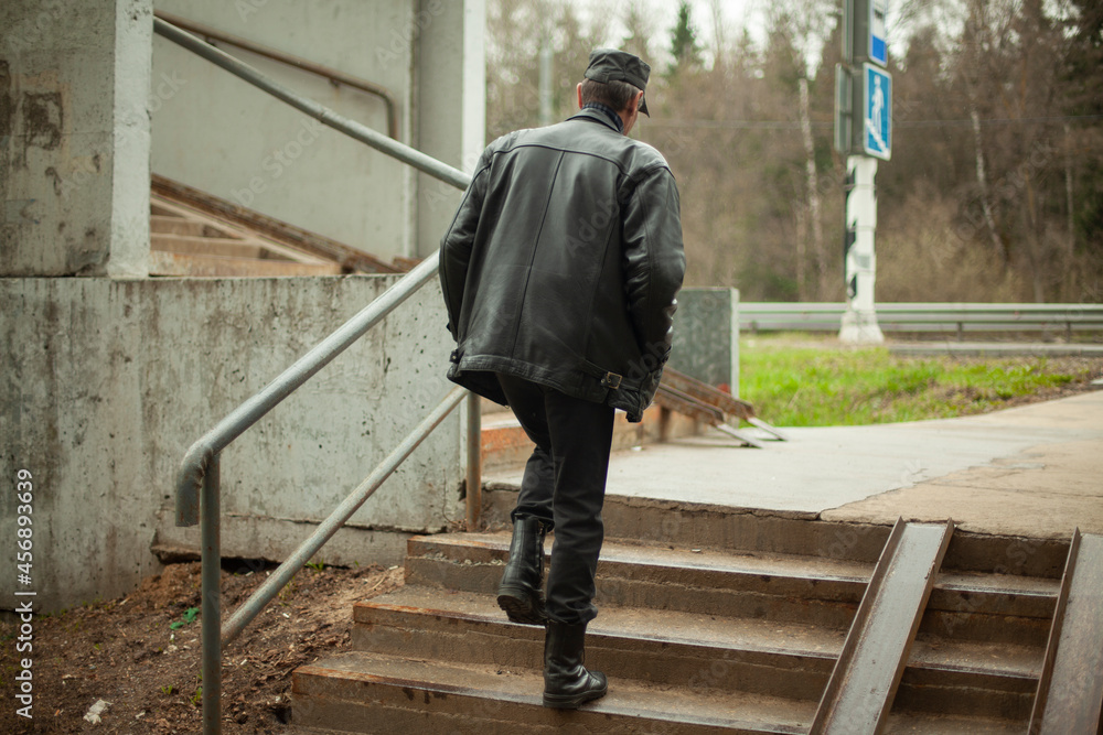 The man climbs the stairs. A person walks up the steps. Old pedestrian crossing. Place of crossing the road. A man in black leather clothes.