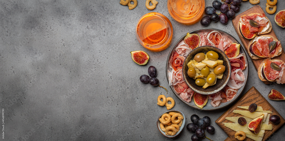 Appetizer with cocktails. Artichoke canned, olives, bruschetta with italian prosciutto cotto, crudo and figs, cheese, grape. Grey surface, copy space.