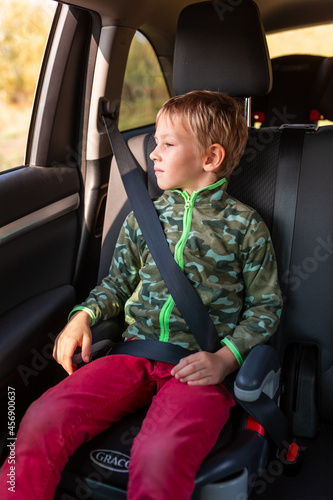 Little boy sitting on a booster seat buckled up in the car.