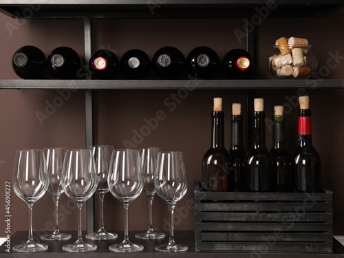 Bottles of wine, corks and glasses on rack near brown wall