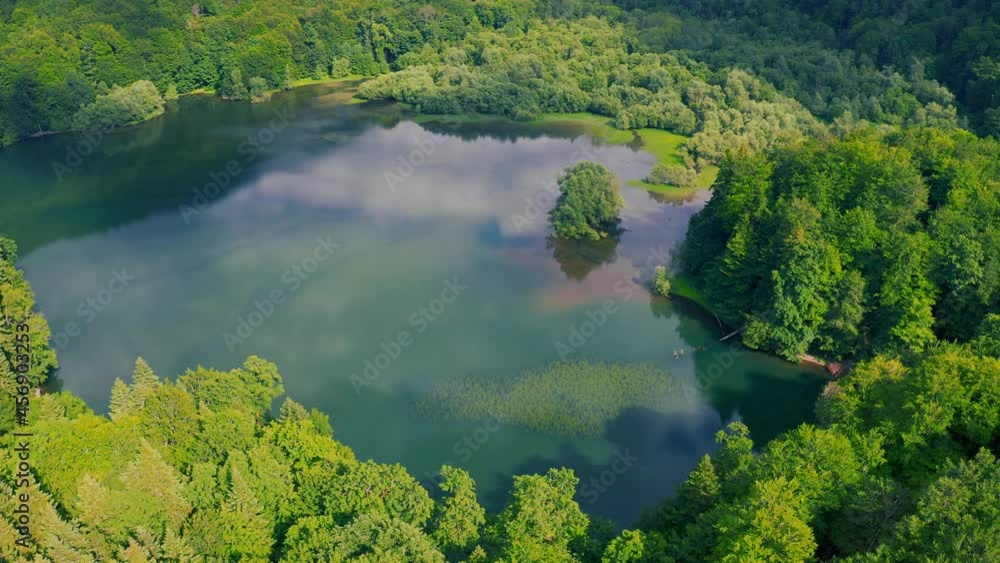 Birds eye view of scenic emerald lake surrounded by pine forests. Clouds reflecting in lake. Aerial view 4K. Birds eye view of scenic emerald lake surrounded by pine forests. Clouds reflecting in lake. Aerial view 4K.