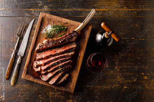 Grilled sliced Tomahawk Steak on bone and glass of Red wine on wooden background