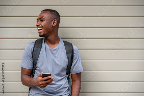 Afro young man using mobile phone against a wall