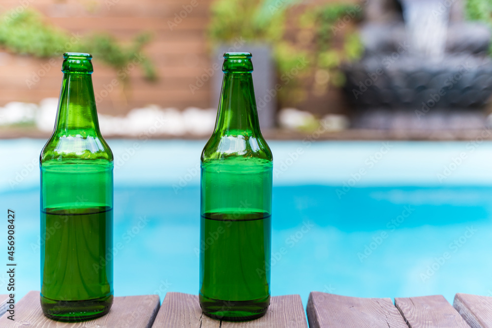 Two green bottles of beer without a logo outside. Swimming pool in the tropics. Alcohol at a patio party. No people Two green bottles of beer without a logo outside. Swimming pool in the tropics. Alcohol at a patio party. No people