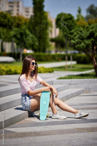 beautiful skateboarder girl with skateboard sitting outdoors