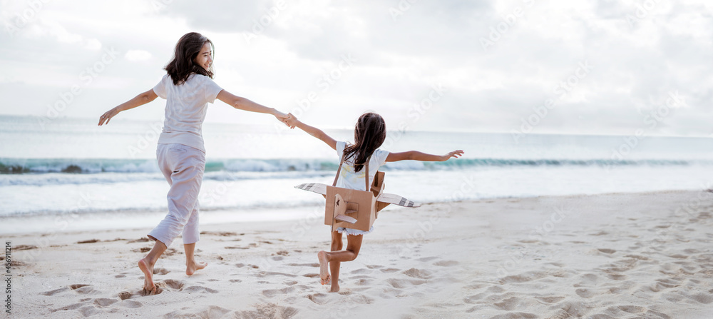 mother and daughter playing with cardboard airplane on the beach together