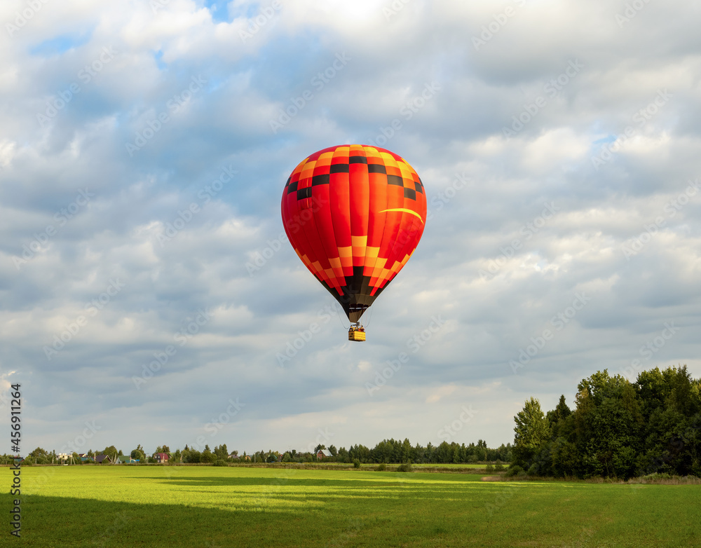 Naklejka premium Big beautiful single hot balloon fly high in the sky over scenery green field and forest. Extreme entertainment for vacation and leisure.