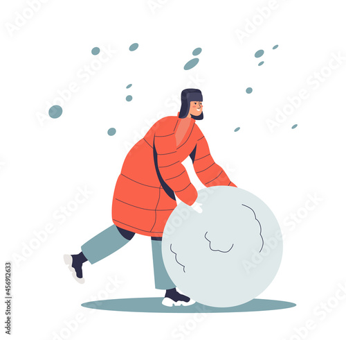 Boy in warm winter clothes making huge snowball for snowman outdoors under snowfall