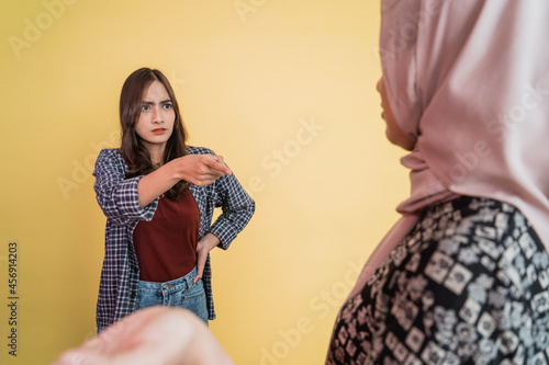 angry woman pointing finger at Muslim woman in hijab with evasive hand gesture photo