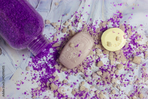 Soap bars lay on a white surface, purple lavender-scented bath sea salt scattered from a plastic bottle on a table flat lay. Spa treatments, relax procedures. Body care, beauty concept. Lilac colors. photo