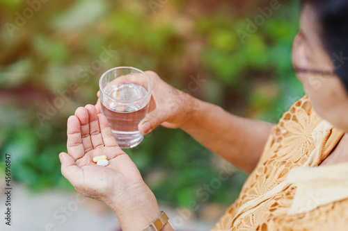 The old woman holds a pill in her hand with a glass of water to eat. Health care concept. photo