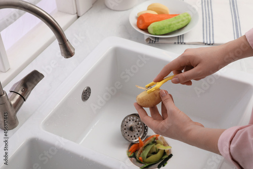 Woman peeling potato over kitchen sink with garbage disposal at home, closeup photo