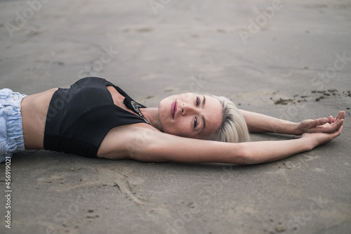 Portrait of beautiful caucasian young woman with blond hair wearing black short top. Laying on the sand on the beach and enjoying. Expressive face 