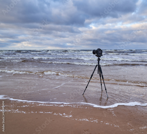 Camera on tripod on the beach. Cloudy weather.