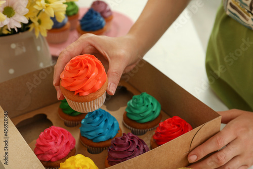 Woman packing box of delicious colorful cupcakes at table, closeup