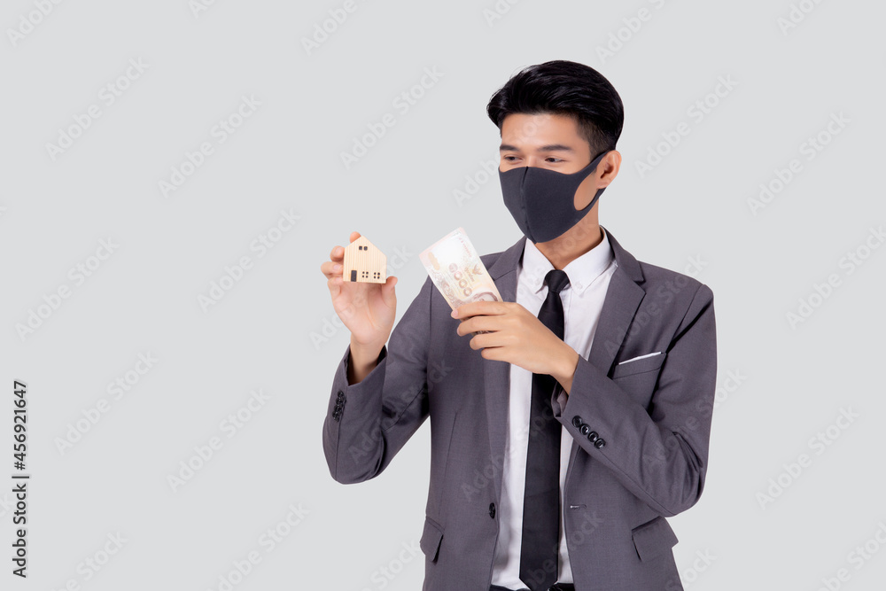 Young asian businessman in face mask holding money Thai and home isolated on white background, pandemic and crisis of economic, business man and investment property during disease covid-19. Young asian businessman in face mask holding money Thai and home isolated on white background, pandemic and crisis of economic, business man and investment property during disease covid-19.