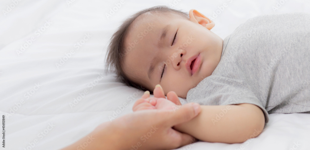 Young asian mother touch hand of little baby girl with tender on bed in the bedroom, mom love newborn and care, woman with expression with child together, parent and daughter, family concept. Young asian mother touch hand of little baby girl with tender on bed in the bedroom, mom love newborn and care, woman with expression with child together, parent and daughter, family concept.