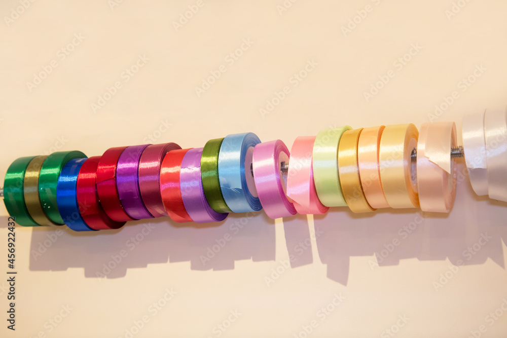 Satin ribbons in rolls of pink, red, green, white color are on the rod, white background. Backgrounds design textures. Satin ribbons in rolls of pink, red, green, white color are on the rod, white background. Backgrounds design textures.