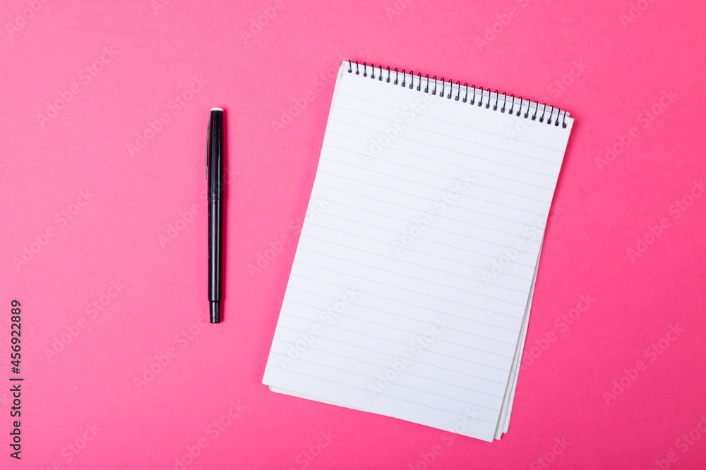 Composition of notebook with copy space and pen on pink background Composition of notebook with copy space and pen on pink background