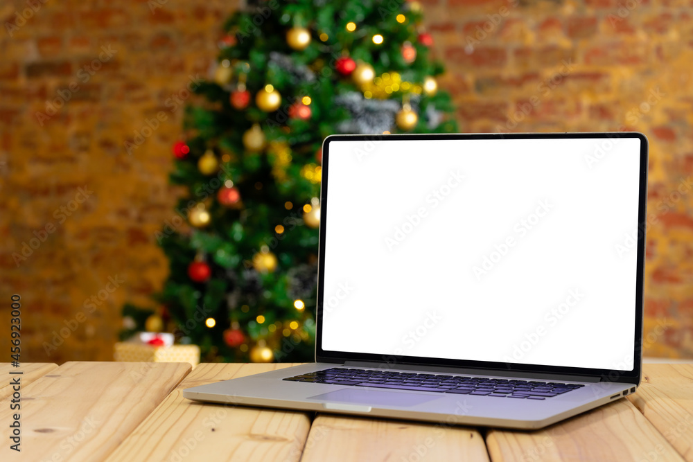Fototapeta premium Composition of laptop with copy space on wooden table with christmas tree in background
