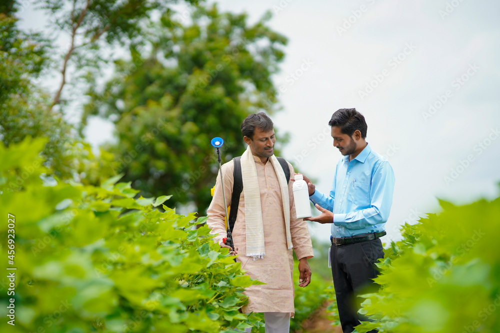 Young indian agronomist giving liquid fertilizer bottle to farmer and saying product information at green agriculture field. Young indian agronomist giving liquid fertilizer bottle to farmer and saying product information at green agriculture field.