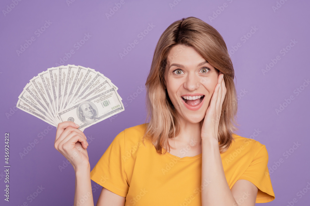 Photo of young pretty woman happy positive smile shocked hold dollars cash rich isolated over violet color background Photo of young pretty woman happy positive smile shocked hold dollars cash rich isolated over violet color background