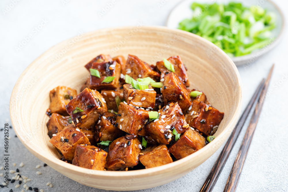 Fried tofu cubes with sauce and sesame seeds in a bamboo bowl, closeup view