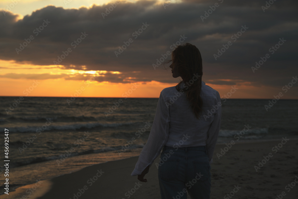 Woman on sandy beach during sunset, back view