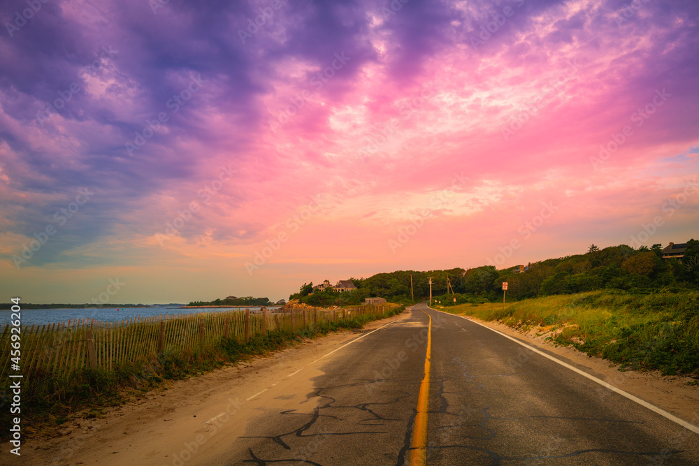 Pink sunrays and purple clouds in the dramatic sky after rain over the Nobska Beach road on Cape Cod, Massachusetts.