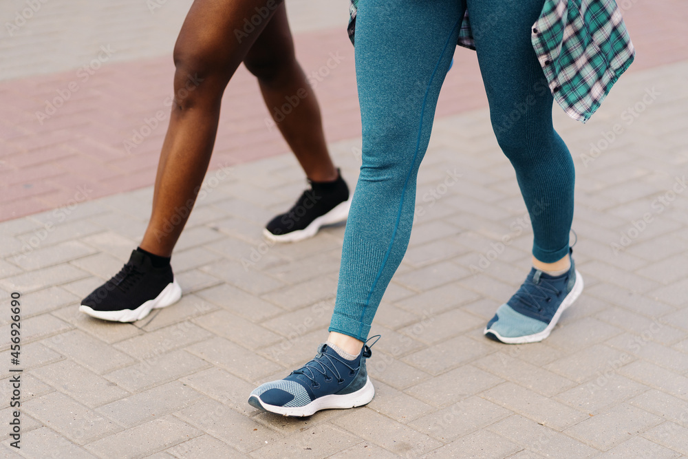 Side view of friends legs in sportswear jogging in the city. Multiethnic women having a fitness workout.