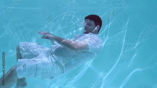 Man in clothes wallows underwater. He sinks into the water.