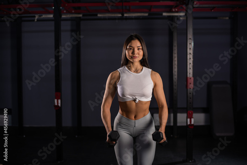 Asian woman doing exercises with dumbbells in the gym. © Михаил Решетников