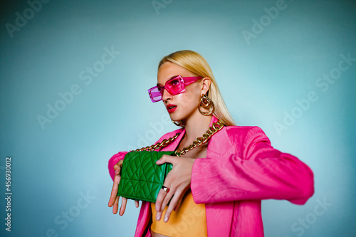 Fashion portrait of confident woman holding trendy green quilted leather bag with chunky chain. Model wearing pink sunglasses, blazer. Accessories advertising conception. Copy, empty space for text photo