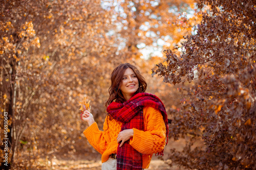 a young woman in an orange sweater wraps herself in a scarf in an autumn park