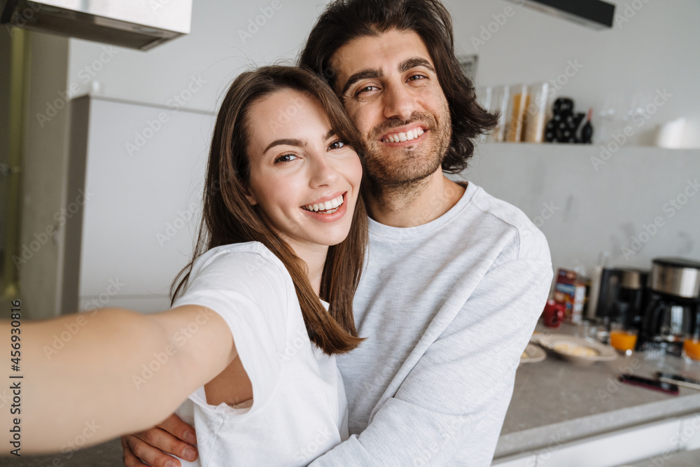 Young multiracial couple laughing and hugging while taking selfie photo Young multiracial couple laughing and hugging while taking selfie photo