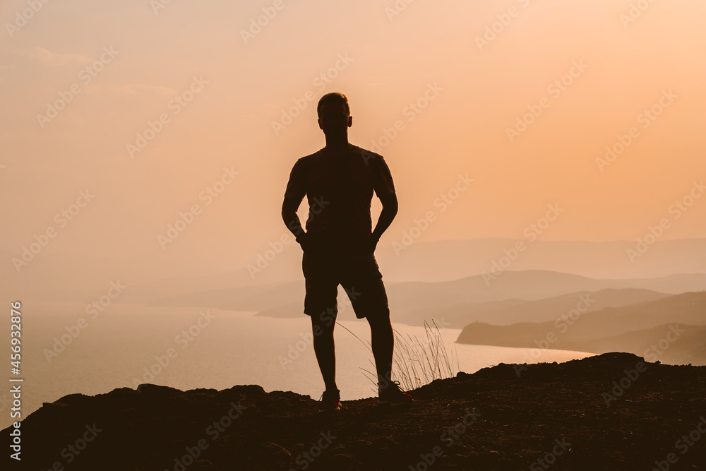 Silhouette of a man at sunset on a cliff with a magnificent landscape and a view of the sea and mountains