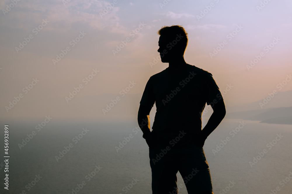 Silhouette of a man at blue sunrise on a cliff with a magnificent landscape and a view of the sea and mountains