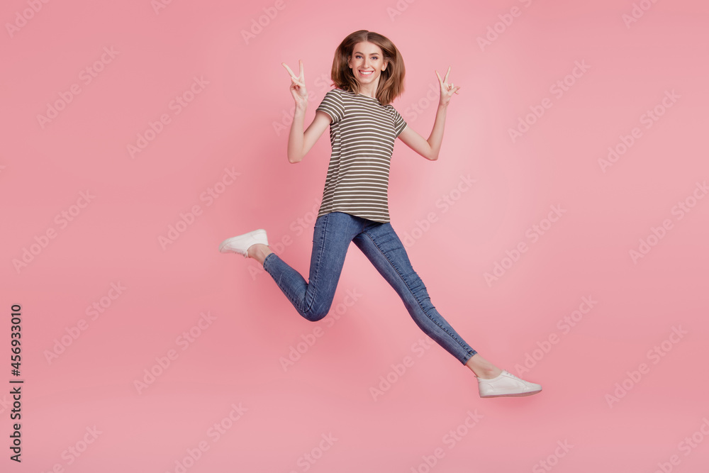 Full length profile side photo of young woman happy positive smile show peace cool v-sign jump isolated over pink color background