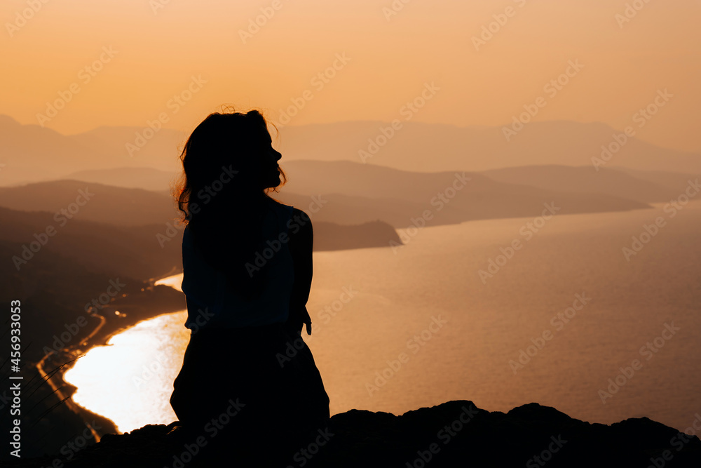 Siluet women at orange sunset on a cliff overlooking the mountains
