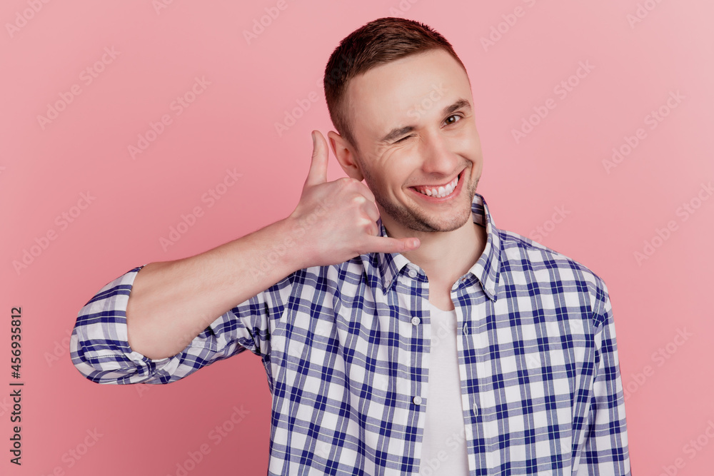 Photo of happy positive smile man make call me gesture phone speak tell wink eye isolated on pink color background Photo of happy positive smile man make call me gesture phone speak tell wink eye isolated on pink color background