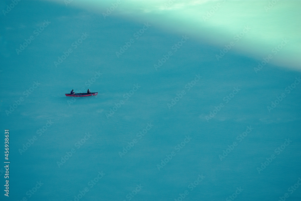 Boat with two people paddling on a cold turquoise mountain lake Boat with two people paddling on a cold turquoise mountain lake