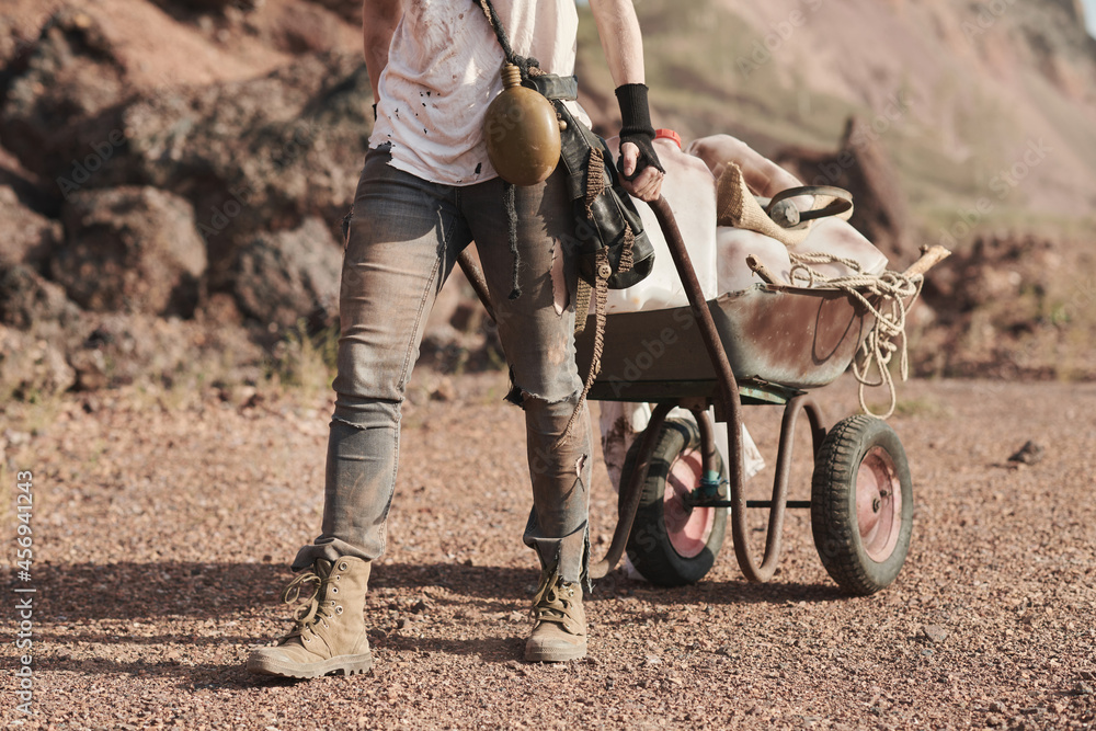 Close-up of female refugee in dirty clothing carrying wheelbarrow with things behind her in the desert Close-up of female refugee in dirty clothing carrying wheelbarrow with things behind her in the desert