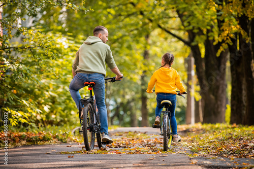 Happy father and daughter ride bicycles in autumn park on sunny day. © Maria Moroz