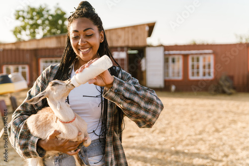 Black woman smiling and feeding goat while working on farm © Drobot Dean