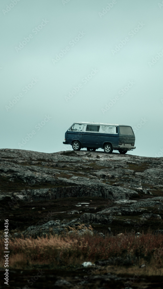 A hippy car stands on the edge of the rocks against the backdrop of a cloudy sky