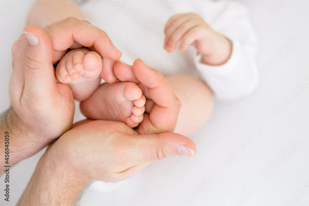 The father holds the tiny legs of a newborn baby in his palms. Gentle and affectionate relations of parents to children. Taking care of children's health from birth. Father's Day The father holds the tiny legs of a newborn baby in his palms. Gentle and affectionate relations of parents to children. Taking care of children's health from birth. Father's Day