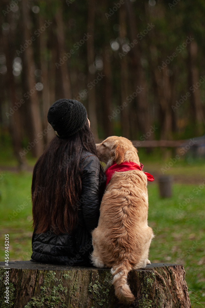 a latina woman sitting on the ground kissing her dog on her back looking at nature a latina woman sitting on the ground kissing her dog on her back looking at nature