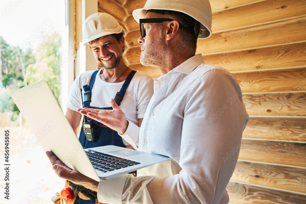 Civil engineer with laptop explaining something to housebuilder Civil engineer with laptop explaining something to housebuilder