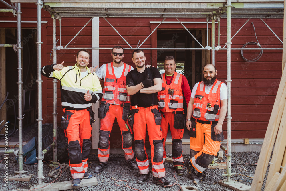 Full length of smiling male construction workers standing together at site Full length of smiling male construction workers standing together at site
